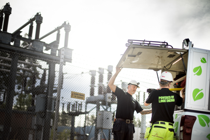 Två drifttekniker lyfter ut verktyg ur en Linde energi-bil framför en transformatorstation